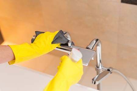 Female hands with yellow rubber protective gloves cleaning bath faucet. Spring cleaningの写真素材