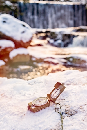 Compass instrument  on the rock with waterfall blurred background. Winter mountain trip concept