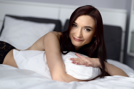 Young brunette woman posing on the bed with white bedding.の写真素材