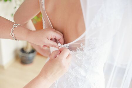 Mother helping the bride - her daughter to put her wedding dress on, close up photoの写真素材