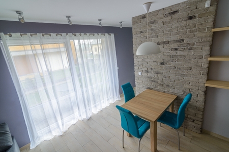 dining room with old grey brick wall, wooden table, turquoise leather chairs and empty shelves. Grey...