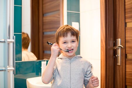Little 7 years old boy brushing his teeth in the bathroom.  Dressed in grey  hooded blouseの写真素材
