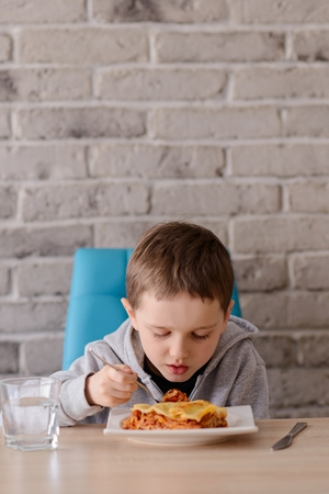 7 years old boy eating lasagne in dining room. Wears grey hoodie.の写真素材