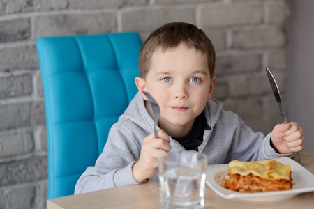7 years old boy eating lasagne in dining room. Wears grey hoodie.の写真素材