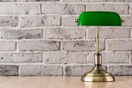 Green and gold banker lamp on the desk with old brick wall backgroundの写真素材