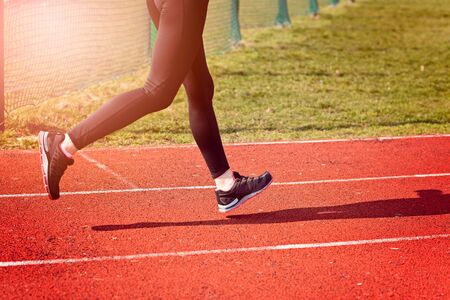 The legs of a woman running around the track on a sunny spring day. Woman running concept.  Runner...
