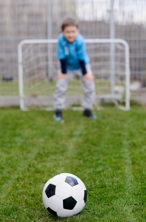 Football ball on grass and little soccer goalkeeper saving the goal. Child playing footballの写真素材