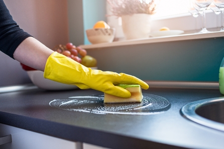 Closeup on woman's hands in yellow protective rubber gloves cleaning kitchen cabinets with sponge.の写真素材