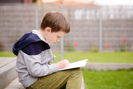 7 year old boy, a student reading a book on the terrace in the gardenの写真素材