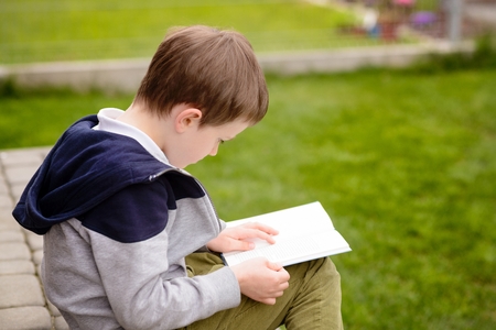 7 year old boy, a student reading a book on the terrace in the gardenの写真素材