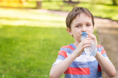 Sweet little boy drinking mineral water from the plastic bottle  in the parkの写真素材