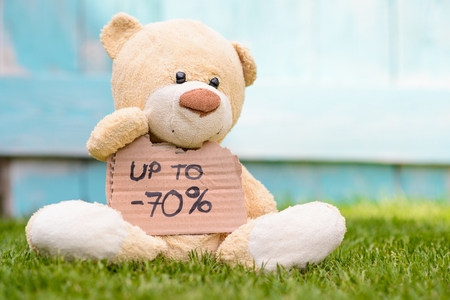 Little old teddy bear sitting on the grass in the garden and holding a piece of cardboard with the information - -70%の写真素材