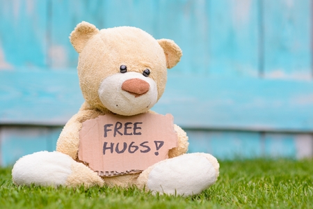 Little old teddy bear sitting on the grass in the garden and holding a piece of cardboard with the information - Free Hugs !の写真素材