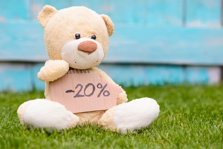 Little old teddy bear sitting on the grass in the garden and holding a piece of cardboard with the information -20%の写真素材