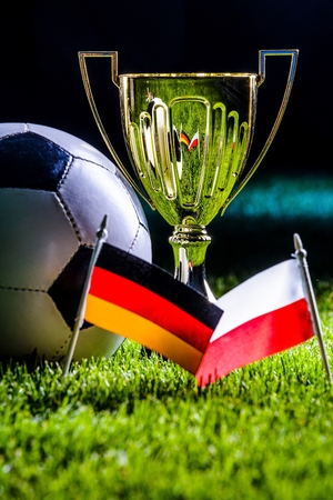 Football cup and Polish and German flags with football ball on grass by nightの写真素材