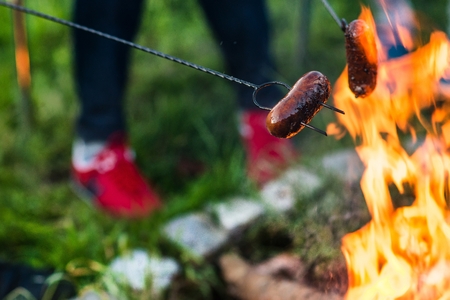 Roasting sausages on campfire with friendsの写真素材
