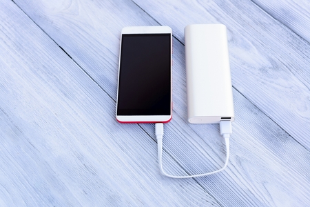 Powerbank charging white and red smartphone - outdoor, wooden backgroundの写真素材