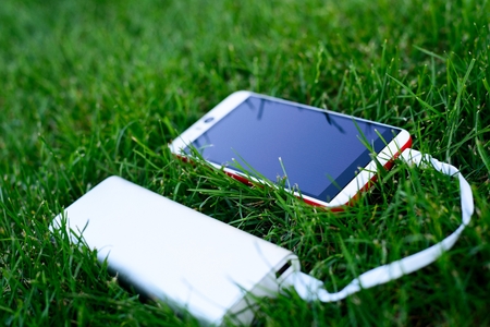 Powerbank charging white and red smartphone - outdoor, grassの写真素材