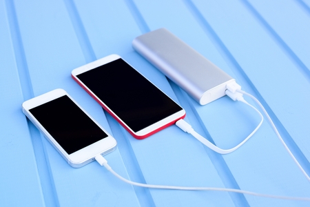 Powerbank charging two smartphones - outdoor, blue wooden backgroundの写真素材