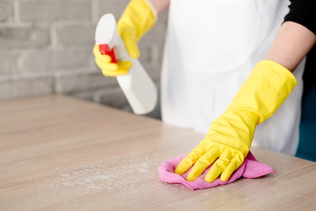 Woman in yellow rubber gloves cleaning table with pink clothの写真素材