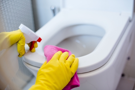 Woman in yellow rubber gloves cleaning toilet with pink clothの写真素材