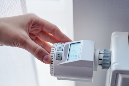 Woman adjusting temperature of home heater in roomの写真素材