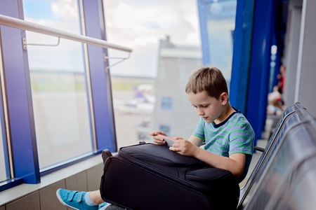Bored 7 years old boy child waiting for his plane at airport and play games on smartphoneの写真素材