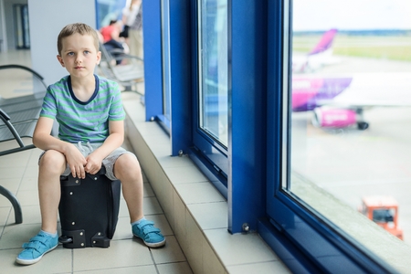 Child sitting at bag at the airport and waiting for his planeの写真素材