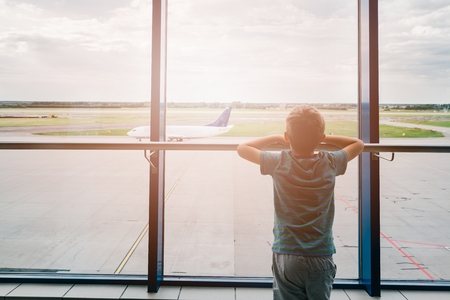 Tired child at the airport, traveling and waiting near window for his plane. Canceled flightの写真素材