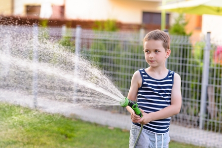 Little boy child watering grass in garden. Summer gardeningの写真素材
