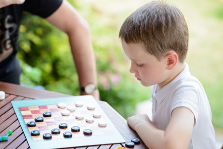 Little boy playing checkers board game with his grandpa on the terraceの写真素材