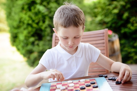 Little boy playing checkers board game on the terraceの写真素材
