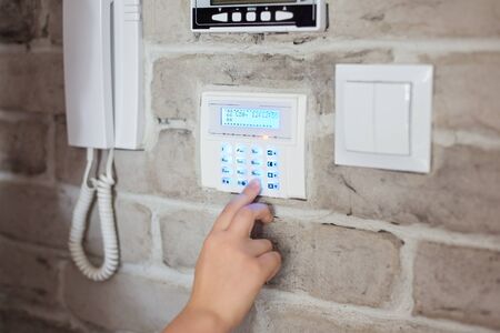 Little baby boy pushes a buttons on the alarm keypad - home security system mounted on wallの写真素材