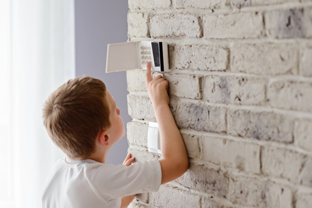 Little baby boy pushes a buttons on the alarm keypad - home security system mounted on wallの写真素材