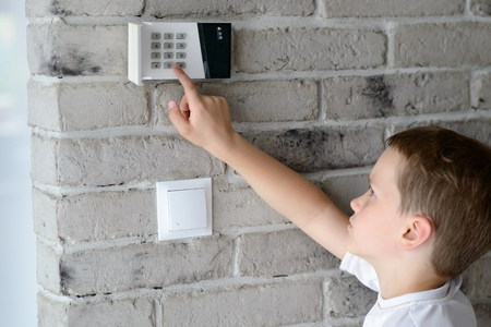 Little baby boy pushes a buttons on the alarm keypad - home security system mounted on wallの写真素材