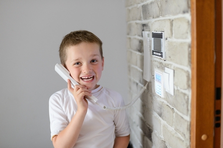 Little baby boy talking on intercom mounted on wallの写真素材