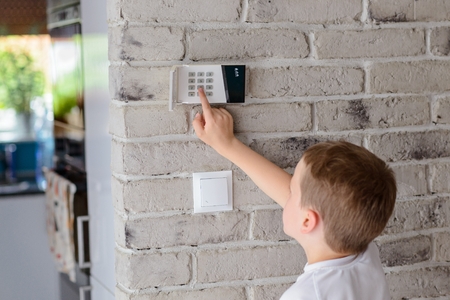 Little baby boy pushes a buttons on the alarm keypad - home security system mounted on wallの写真素材