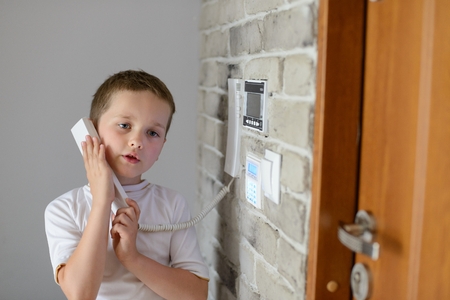 Little baby boy talking on intercom mounted on wallの写真素材