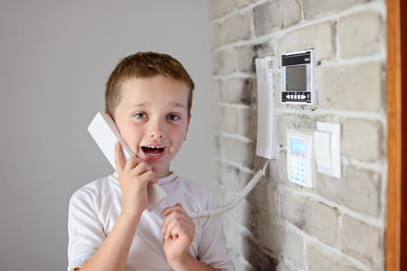Little baby boy talking on intercom mounted on wallの写真素材