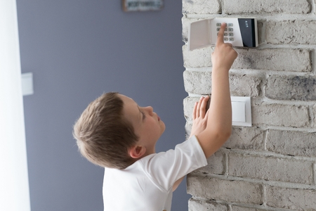 Little baby boy pushes a buttons on the alarm keypad - home security system mounted on wallの写真素材