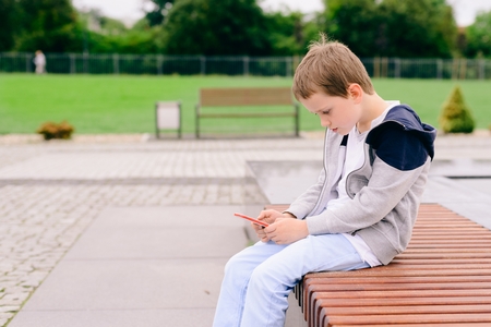 Little boy child playing mobile games on smartphone in the park.の写真素材