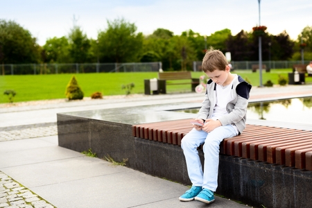 Little boy child playing mobile games on smartphone in the park.の写真素材