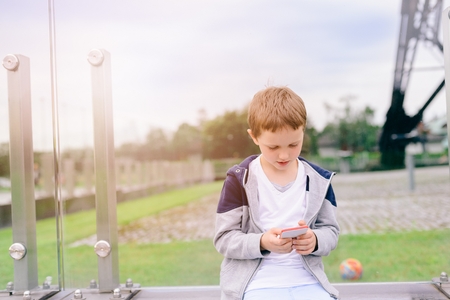 Little boy child playing mobile games on smartphone in the park.の写真素材