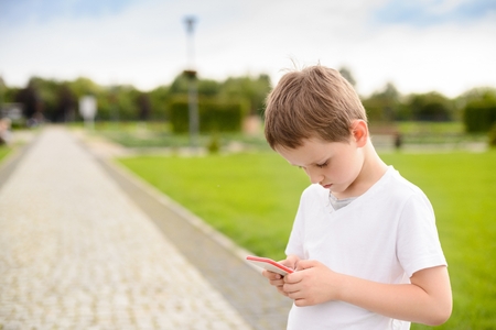 Little boy child playing mobile games on smartphone in the park.の写真素材