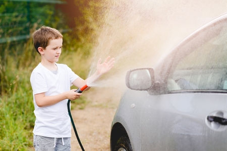 Little boy washing silver car in the garden. Summerの写真素材