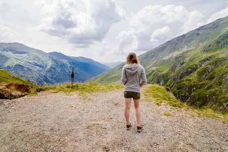 Young woman standing with on cliff's edge and looking on Romanian Carpathian mountainsの写真素材