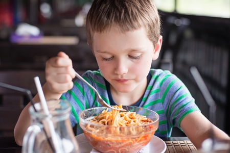 Little 7 years old boy child eating spaghetti bolognese in the restaurantの写真素材