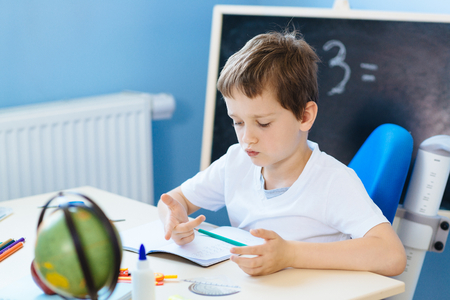 Seven years old boy, counting on fingers while doing his homework. Back to school