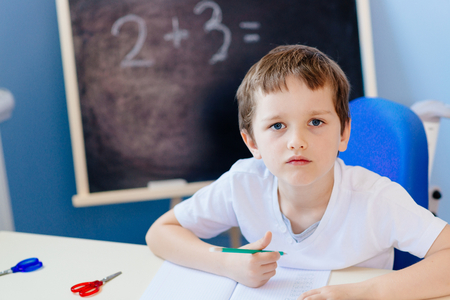 Little 7 years old boy solves multiplication table. Dressed in white t shirt.の写真素材