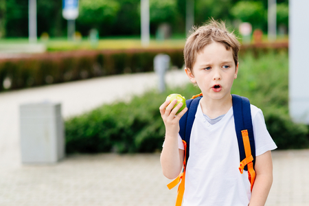 Little 7 years old boy with apple at road to school. Dressed in white t shirt and shortsの写真素材